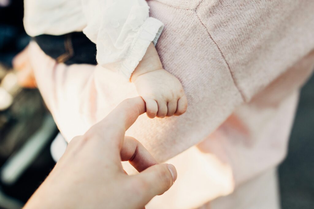 baby holding hand with parent in mom's arms